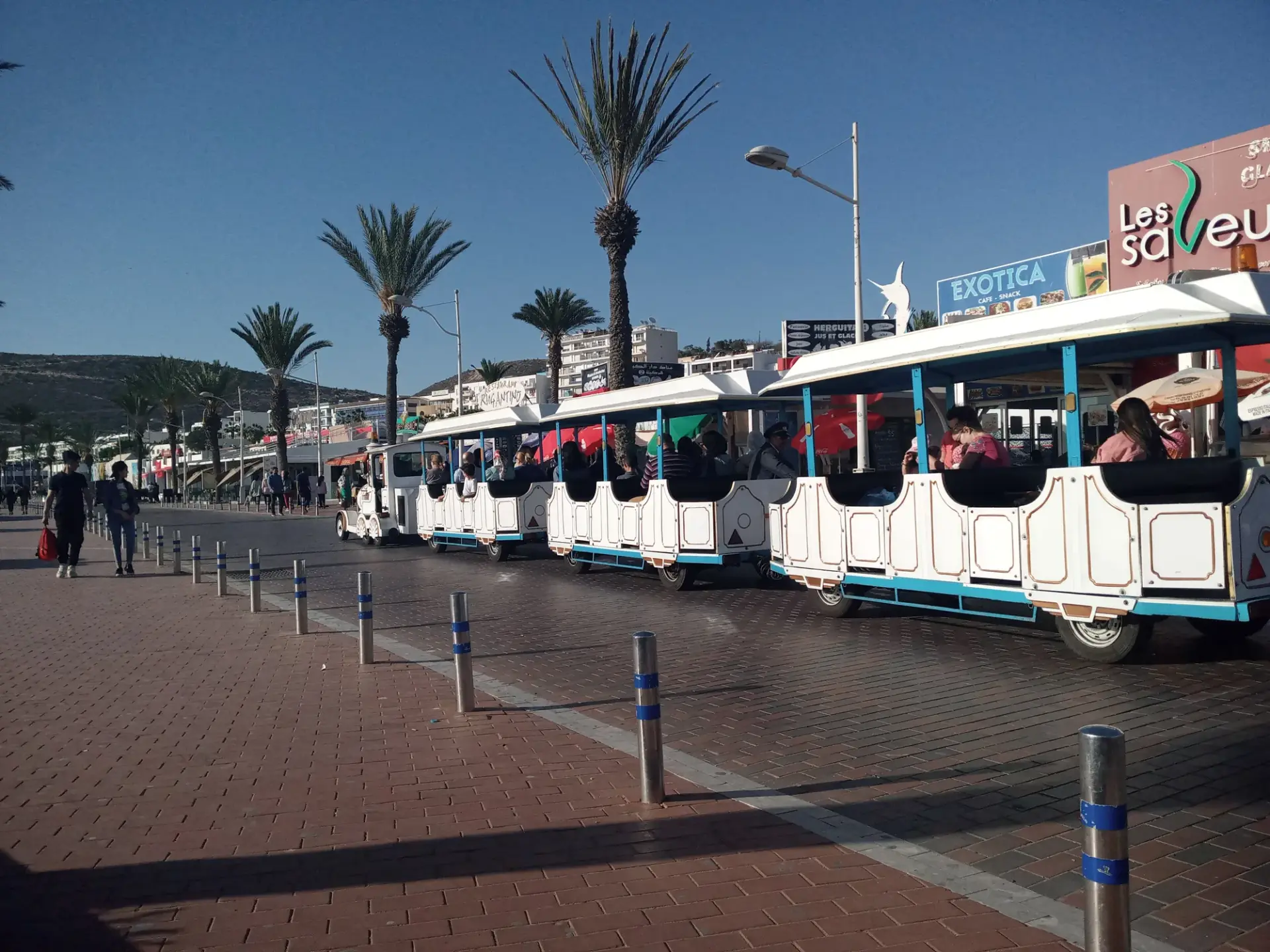 Airport shuttle train waiting on a palm-lined street in Agadir